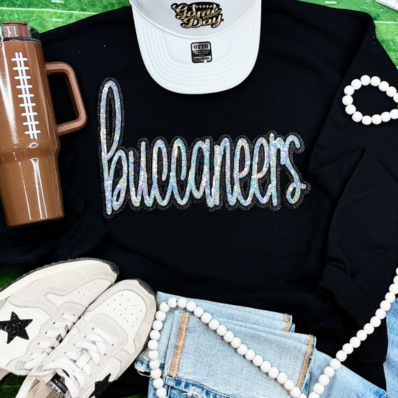Buccaneers Sequin Patch, colorful glittery patch on a black t-shirt with casual accessories including white sneakers, a white cap, a brown tumbler, a pearl necklace, and denim shorts.