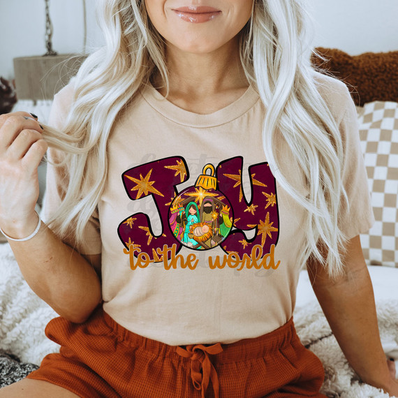 Joy To The World Nativity Scene DTF Heat Transfer, vibrant nativity scene graphic on a beige T-shirt featuring baby Jesus, Mary, Joseph, and the Wise Men with stars and festive text.