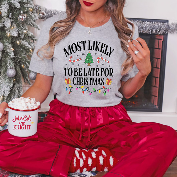 Most Likely To Be Late For Christmas Festive DTF Heat Transfer, Christmas themed graphic on a woman's gray t-shirt with holiday decorations.