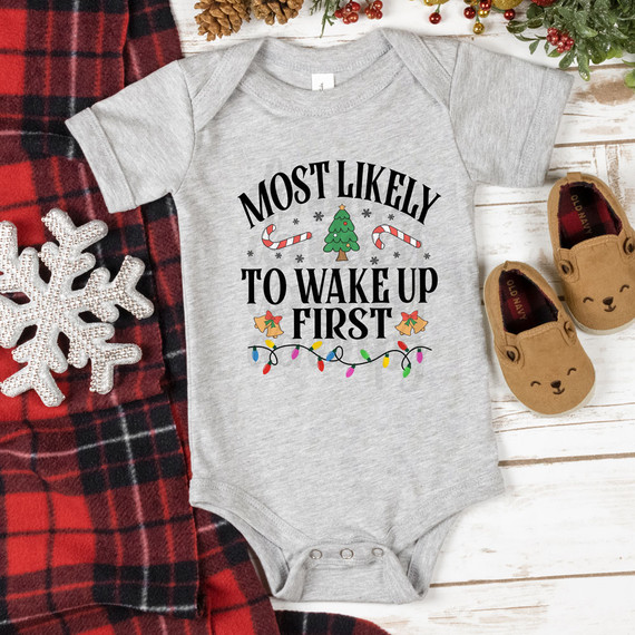 Most Likely To Wake Up First Festive DTF Heat Transfer, a gray baby onesie with holiday-themed print and colorful Christmas lights, candy canes, and Christmas tree design.