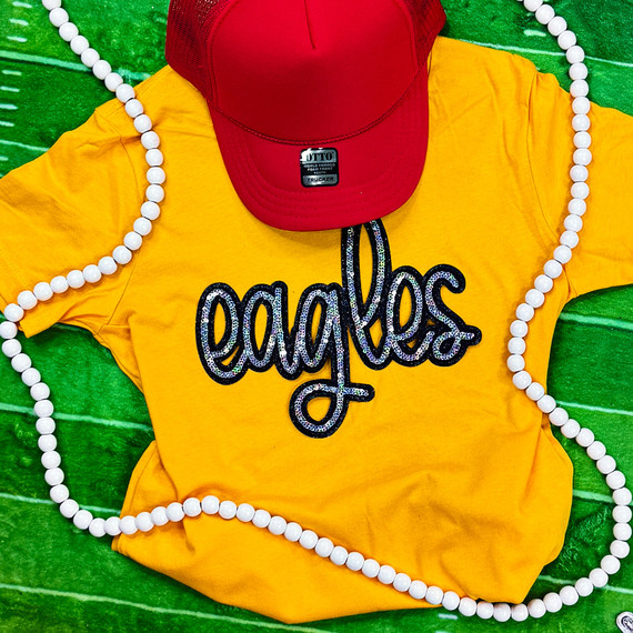 Eagles YOUTH Sequin Patch, colorful yellow T-shirt with the word 'eagles' in black sequins embroidered design, red cap, white beaded necklace, and green background.