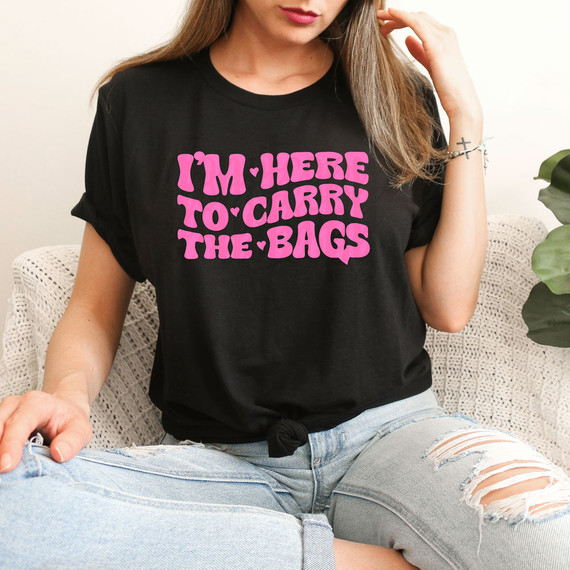 I'm Here To Carry The Bags DTF Heat Transfer, woman wearing a black T-shirt with pink text