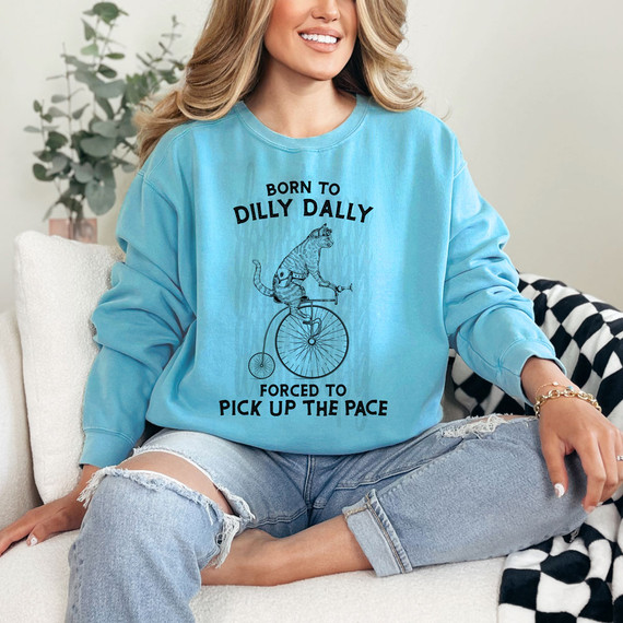 Born To Dilly Dally DTF Heat Transfer, a humorous graphic sweatshirt featuring a cat riding a bicycle, with text 'Born To Dilly Dally, Forced To Pick Up The Pace' for casual wear.