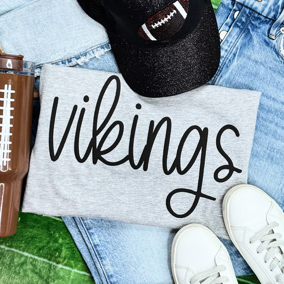 Vikings Black PUFF Screen Print Heat Transfer, black and grey fabric with text design, sneakers, denim shorts, and a football cap.