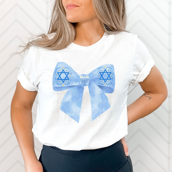 Coquette Hanukkah Bow DTF Heat Transfer, image of a woman wearing a white T-shirt with a blue Hanukkah-themed bow design featuring Hanukkah symbols and menorah in the center.