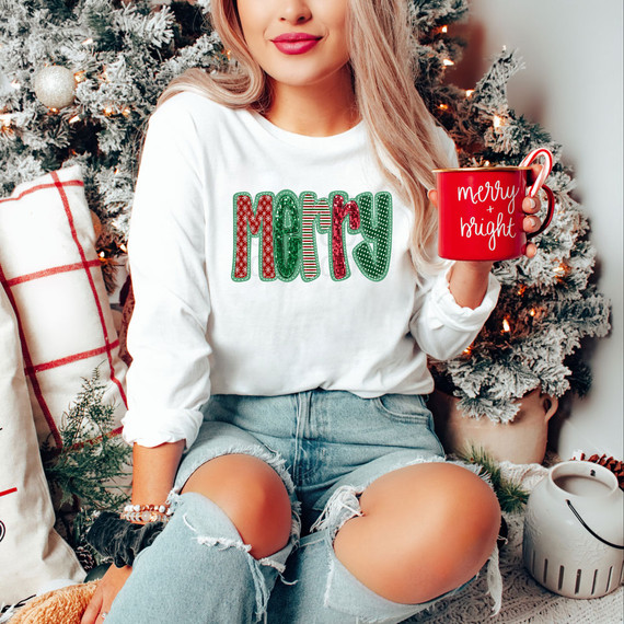 Merry Patchwork Faux Sequins DTF Heat Transfer, close-up of woman's white sweatshirt with festive red and green sequin design spelling 'MERRY' and a woman holding a red mug with 'merry and bright' text, Christmas tree in background.