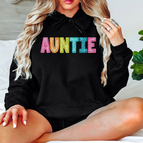 Bright Groovy Auntie Faux Sequins DTF Heat Transfer, colorful glittering 'AUNTIE' text on a black hoodie worn by a woman.
