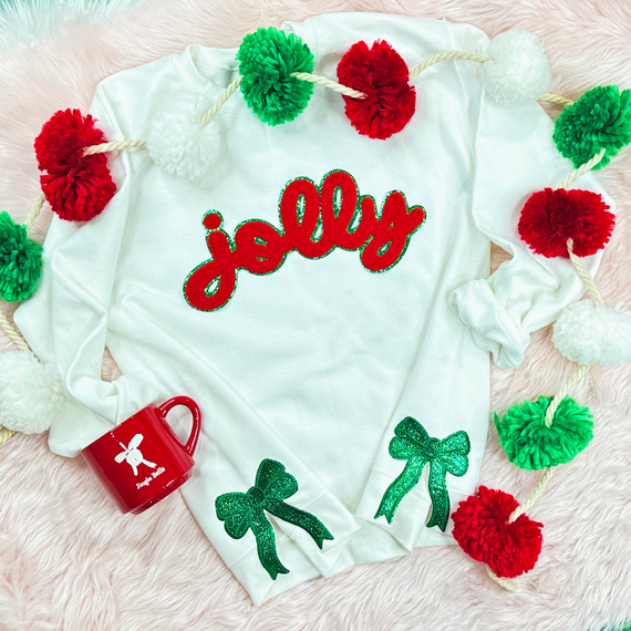 Green Glitter Bow Sides Sequin Patch SET OF 2, festive holiday sweater with green glitter bows and sequins on white fabric surrounded by red, green, and white pom-pom garland and a red mug.