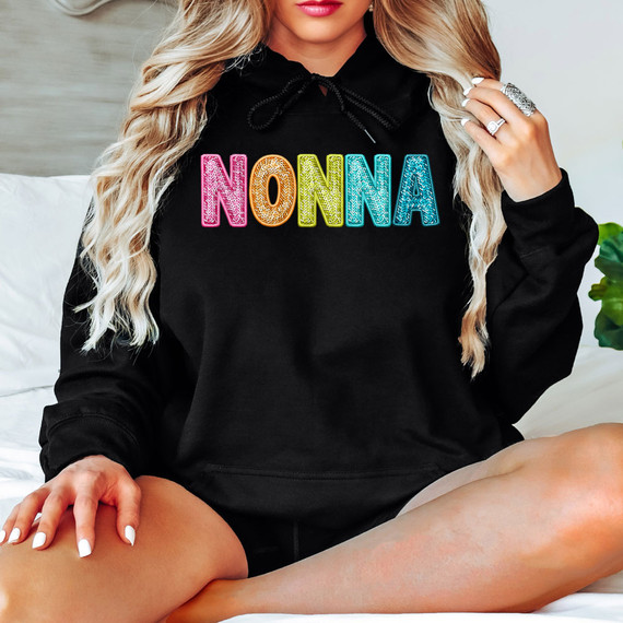 Bright Groovy Nonna Faux Sequins DTF Heat Transfer, colorful sequin embellishment spelling 'NONNA' on a black hoodie worn by a woman with blonde hair.