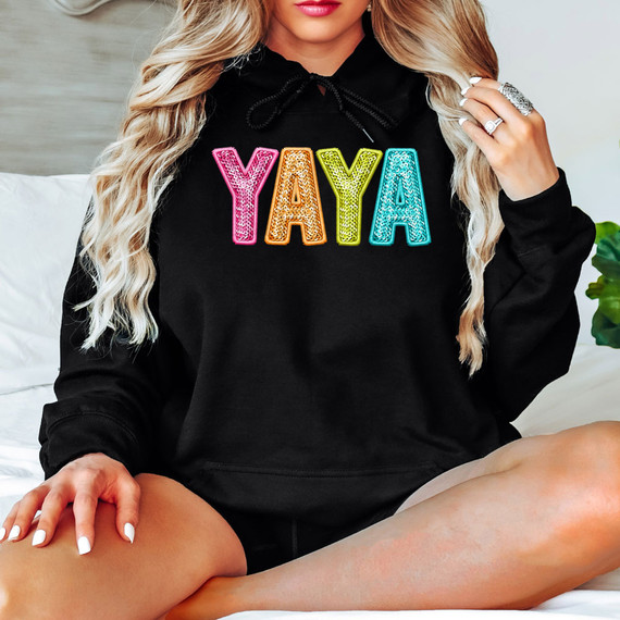 Bright Groovy Yaya Faux Sequins DTF Heat Transfer, a colorful sequin design spelling 'YAYA' on a black hoodie worn by a woman, with vibrant and shiny embellishments.