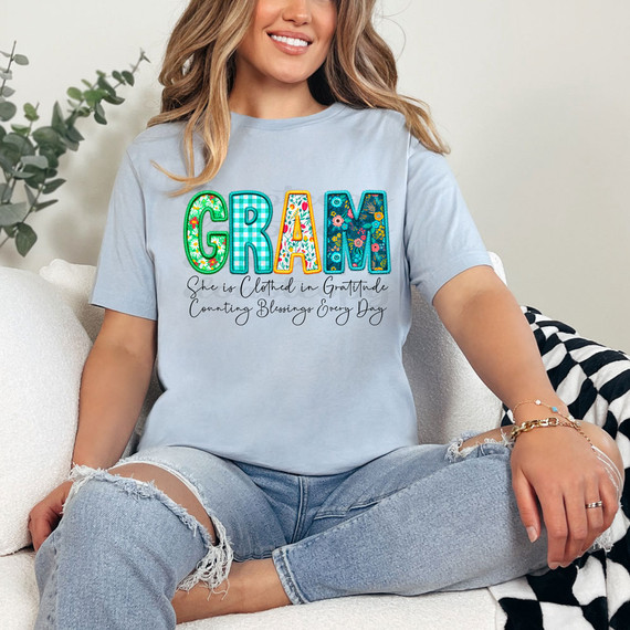 Gram She Is Clothed In Gratitude Counting Blessings Every Day DTF Heat Transfer, T-shirt featuring colorful floral embroidered-style alphabet letters spelling 'GRAM' with the phrase 'She is Clothed in Gratitude, Counting Blessings Every Day' underneath.