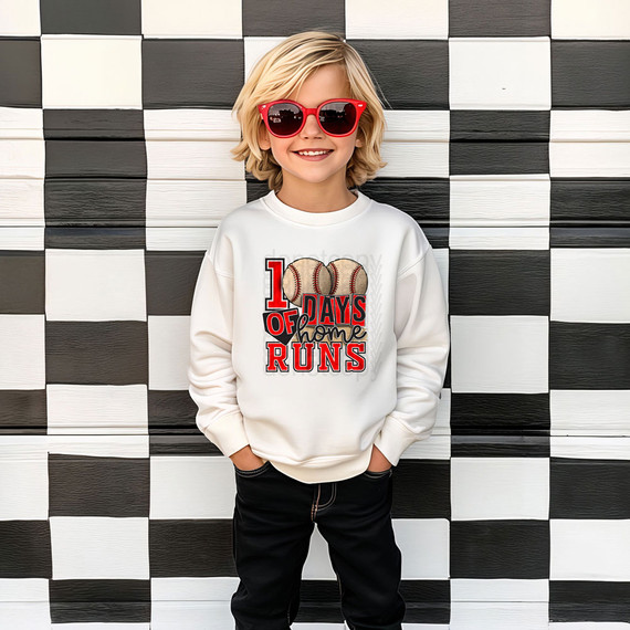 100 Days Of Home Runs DTF Heat Transfer, a young boy wearing a white sweatshirt with a baseball design and text, standing against a black and white checkered background.