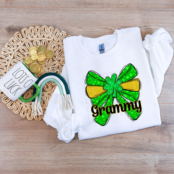 Grammy St Patrick's Day Coquette Bow DTF Heat Transfer, colorful green and yellow bow design with shamrock, on a white T-shirt, with gold coins, a mug, and rainbow necklace nearby.