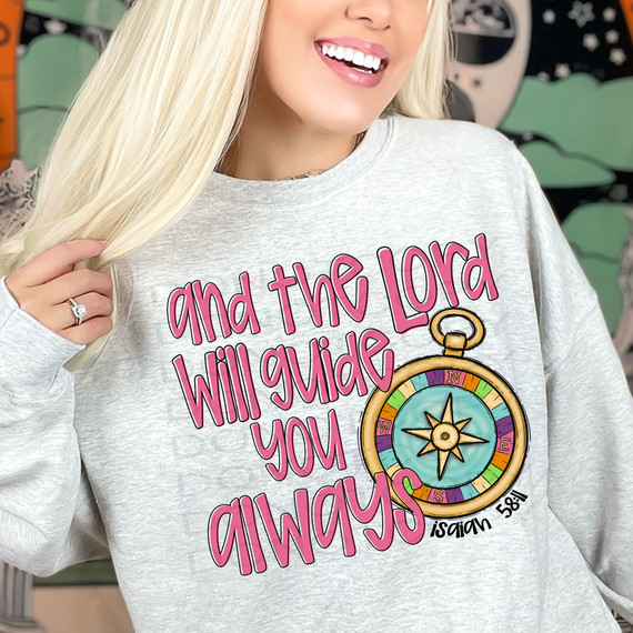 And The Lord Will Guide You Always DTF Heat Transfer, close-up of a person wearing a light grey sweatshirt with a colorful compass design and pink text.