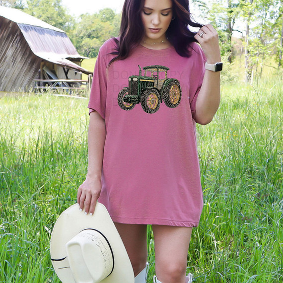 Faux Rhinestone Tractor DTF Heat Transfer, Sparkling black and gold tractor design made with rhinestones on a pink T-shirt worn by a woman outdoors.