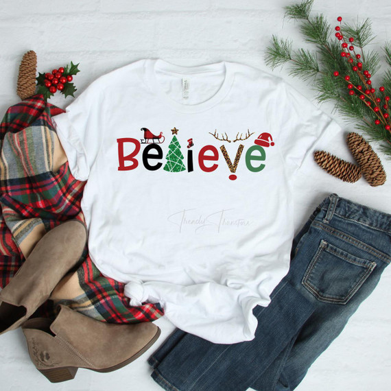 Believe Christmas T-shirt, white T-shirt with festive holiday design including Christmas tree, Santa, reindeer antlers, and holiday hat.