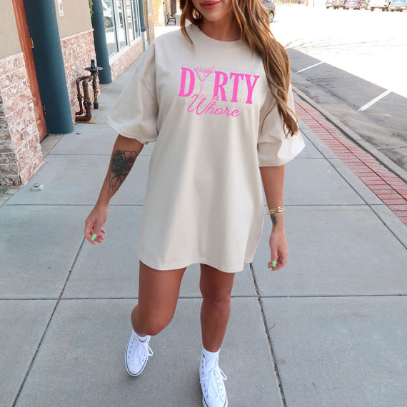 Dirty Whore Martini DTF Heat Transfer, a creative pink graphic design on a beige oversized t-shirt worn by a woman walking on the sidewalk.