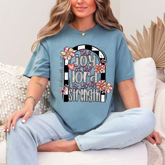 The Joy Of The Lord Is Your Strength Retro Flowers DTF Heat Transfer, a colorful religious-themed design with flowers and text on a blue t-shirt worn by a woman sitting on a sofa.