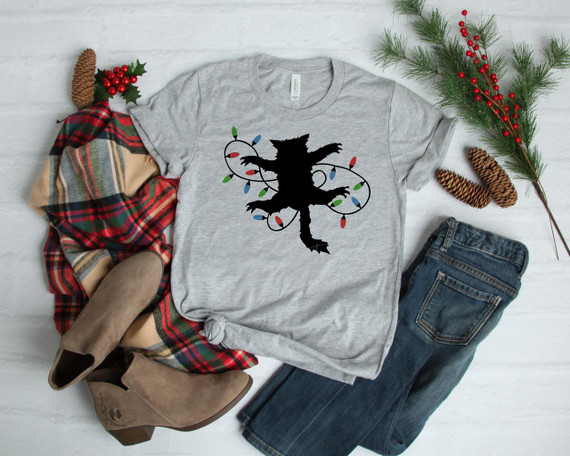 Fried Pussy Cat Sublimation Transfer, a black cat silhouette wrapped in colorful Christmas lights on a gray T-shirt, with holiday decorations including pinecones, holly berries, and a plaid scarf around it.