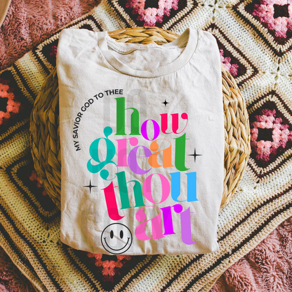 How Great Thou Art DTF Heat Transfer, colorful and artistic printed T-shirt with the phrase 'My savior God to thee, how great thou art' and a smiley face, on a woven and crochet blanket.