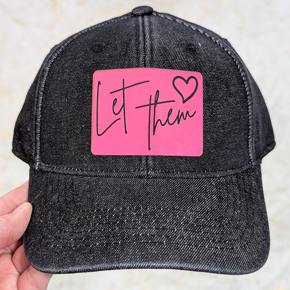 Let them FAUX Leather Patch, black baseball cap with a pink patch that has 'Let them' written in black script and a small heart next to it.