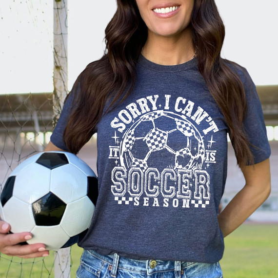 Sorry I Can't It Is Soccer Season WHITE DTF Heat Transfer, woman wearing navy t-shirt holding a soccer ball with a soccer-themed graphic design.