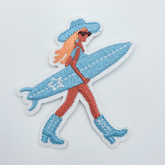 Surfer Cowgirl Embroidered HAT/POCKET Patch, embroidered patch featuring a cowgirl surfing with a blue surfboard, wearing a sun hat and boots.