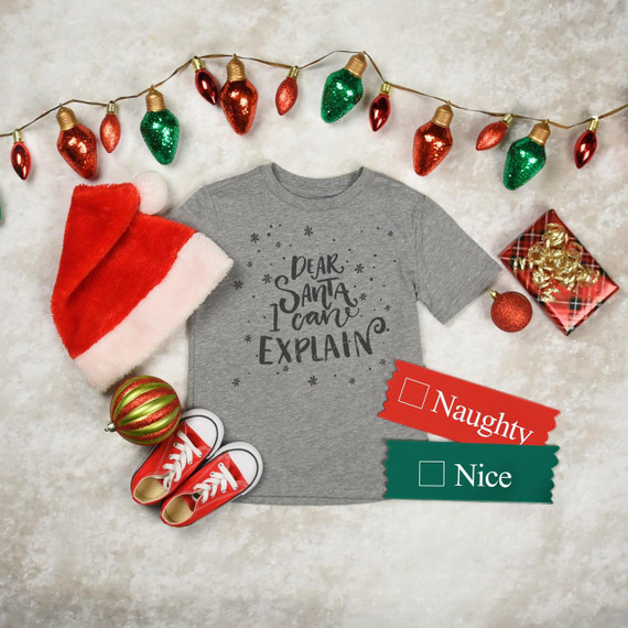 Dear Santa I Can Explain Sublimation Transfer, gray T-shirt with humorous Christmas message, surrounded by holiday decorations including a Santa hat, red sneakers, Christmas ornaments, string lights, and wrapped gifts.