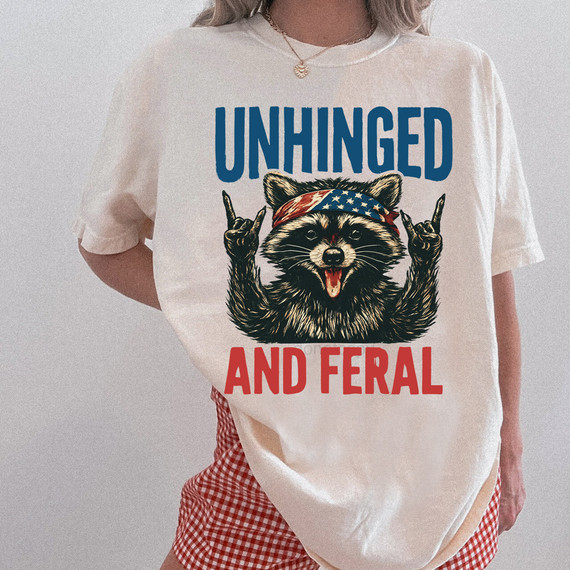 Unhinged And Feral Patriotic Raccoon DTF Heat Transfer, humorous raccoon graphic with patriotic headband and rebellious gesture on a white t-shirt.
