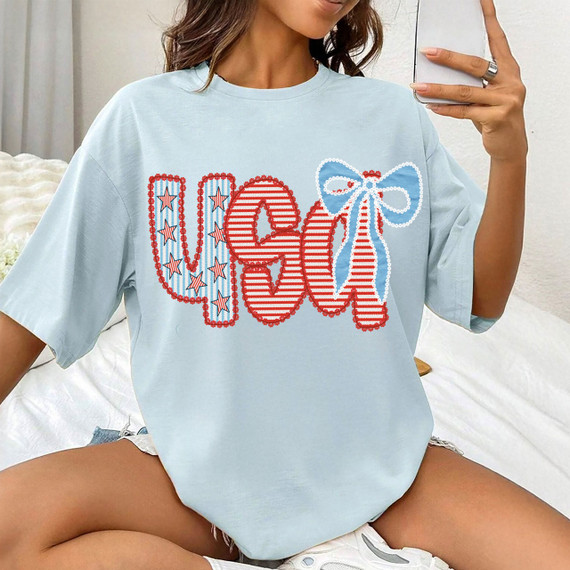 Patterned USA Coquette DTF Heat Transfer, colorful and patriotic design with stars, stripes, and a bow on a light blue T-shirt.