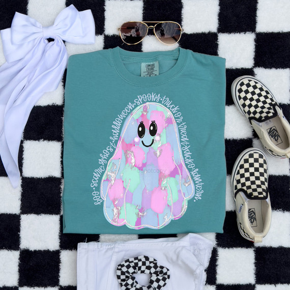 Brushstroke Ghost DTF Heat Transfer, colorful ghost design with pastel colors and a smiley face on a teal t-shirt, surrounded by accessories on a black and white checkered background.