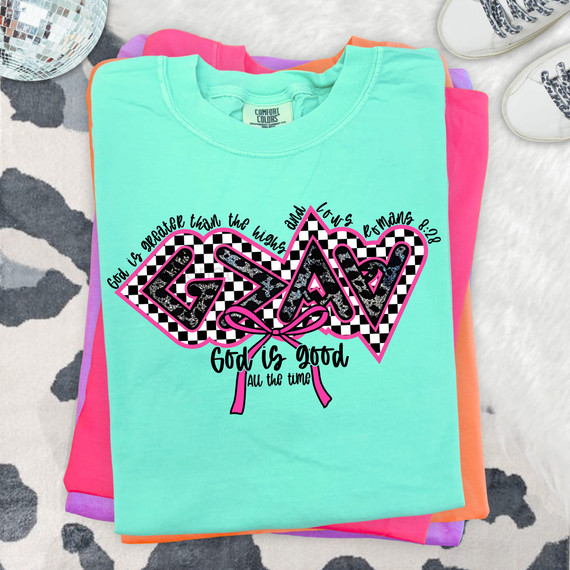 God Is Greater Checkered DTF Heat Transfer T-shirt, colorful graphic design with checkered pattern and motivational quote, stacked on pastel-colored shirts.