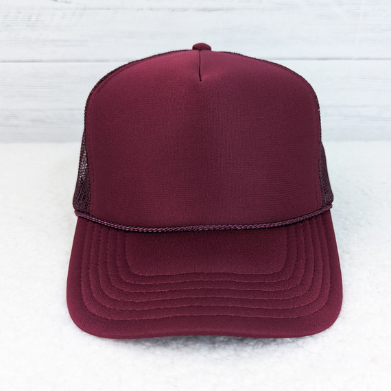 Maroon Foam Trucker Hat, front view of a maroon mesh trucker cap with foam front panel and curved brim set against a white wooden background.