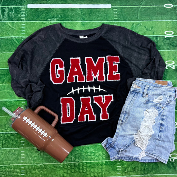 Game Day with Silicon Laces Patch - 10 Colors, apparel set includes a black sweatshirt with red and white 'Game Day' patch, distressed denim shorts, and a football-themed tumbler, on a green football field background.