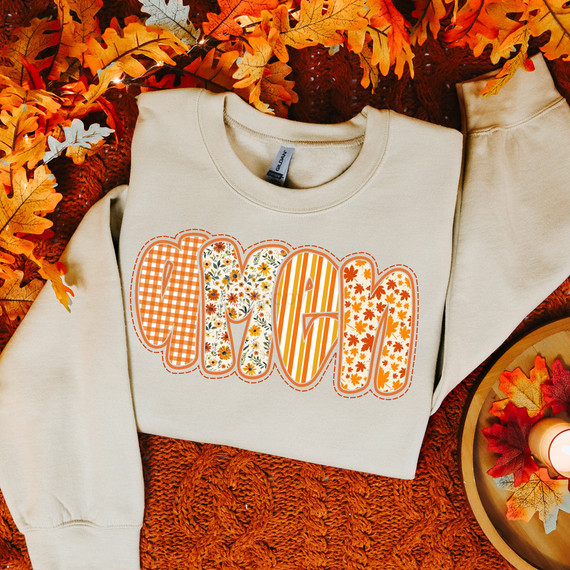Amen Fall Pattern DTF Heat Transfer, beige sweatshirt with fall-themed patterned word "AMEN" in orange, yellow, and white autumn-inspired designs, surrounded by autumn leaves and cozy fall decor.