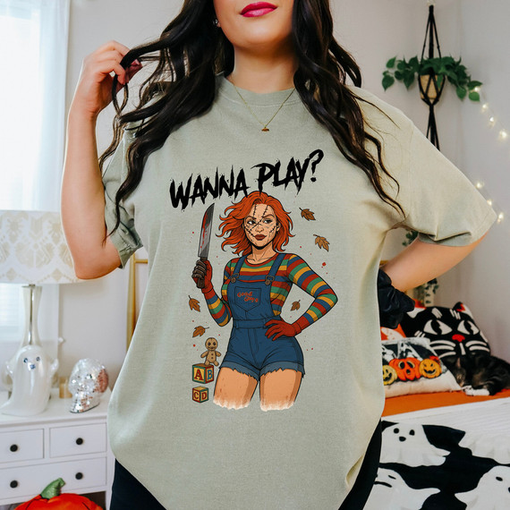 Wanna Play? Doll DTF Heat Transfer, a graphic t-shirt featuring a horror-themed illustrated girl holding a bloody knife, with the text Wanna Play? and playful autumn leaves around.