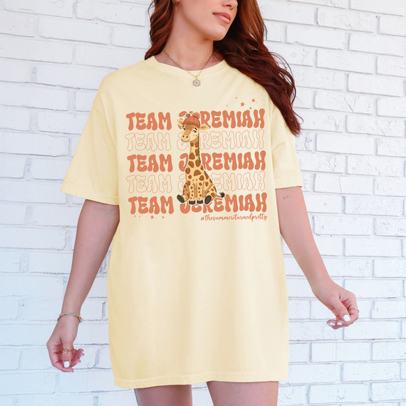 Team Jeremiah Giraffe DTF Heat Transfer, a graphic design of a cute giraffe wearing a hat with the text 'Team Jeremiah' repeated multiple times in bold, playful font on a yellow t-shirt.