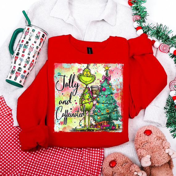 Jolly and Caffeinated DTF Heat Transfer, Festive holiday design on red sweatshirt featuring the Grinch holding a coffee cup and a decorated Christmas tree.