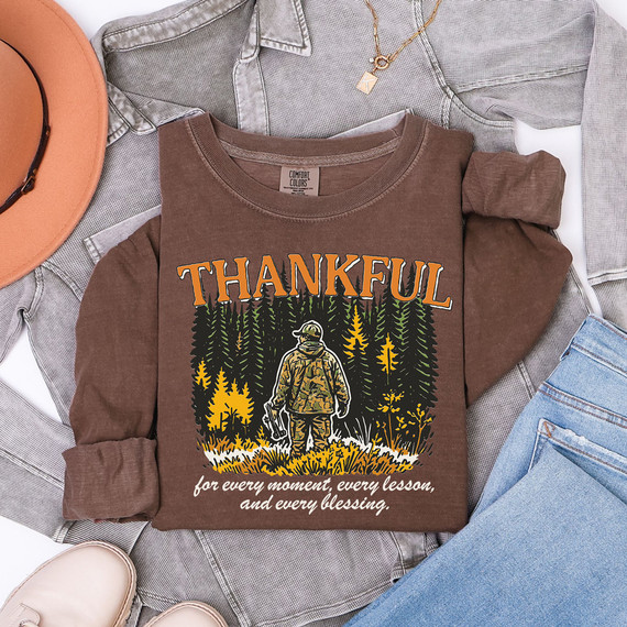 Thankful For Every Moment, Every Lesson, And Every Blessing DTF Heat Transfer, brown sweatshirt with outdoor graphic and text, surrounded by casual clothing and accessories.