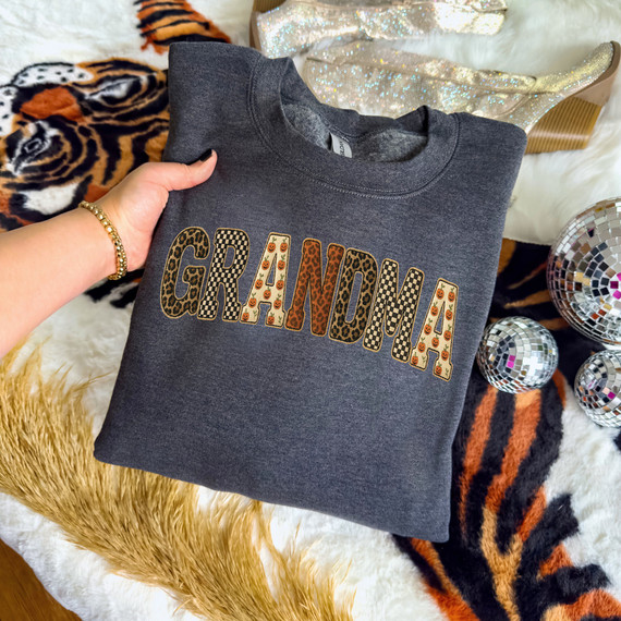 Spooky Patterned Grandma DTF Heat Transfer, dark gray sweatshirt with the word 'GRANDMA' in multicolored, Halloween-themed patterned lettering.