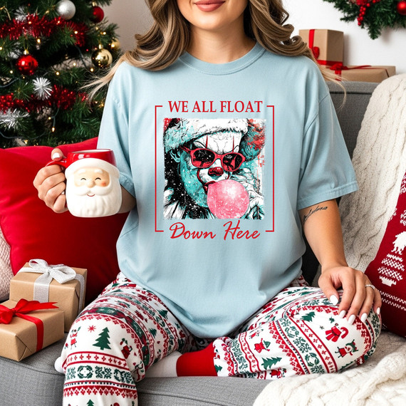 Float Down Here Christmas DTF Heat Transfer, image of a woman wearing a holiday-themed t-shirt with a graphic of a dog with sunglasses and blowing bubblegum, surrounded by Christmas decorations.