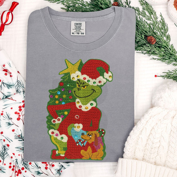 Faux Yarn Green Guy & Max DTF Heat Transfer, Christmas-themed graphic on a gray T-shirt featuring the Grinch with a Christmas tree and a dog, decorated with colorful ornaments and a Santa hat.
