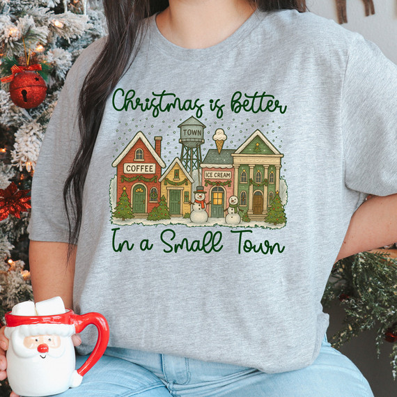 Snowy Christmas Is Better In A Small Town DTF Heat Transfer, illustrated holiday scene on a gray T-shirt with small town buildings, snowmen, and Christmas decorations.