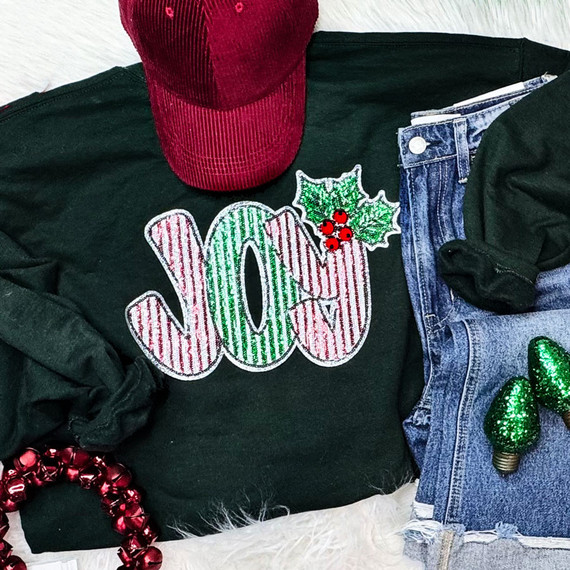 Striped JOY Holly Sequin Patch, festive holiday-themed clothing with a sequin Holly leaf and berries patch on a black sweatshirt, accompanied by a red velvet cap and holiday decorations.