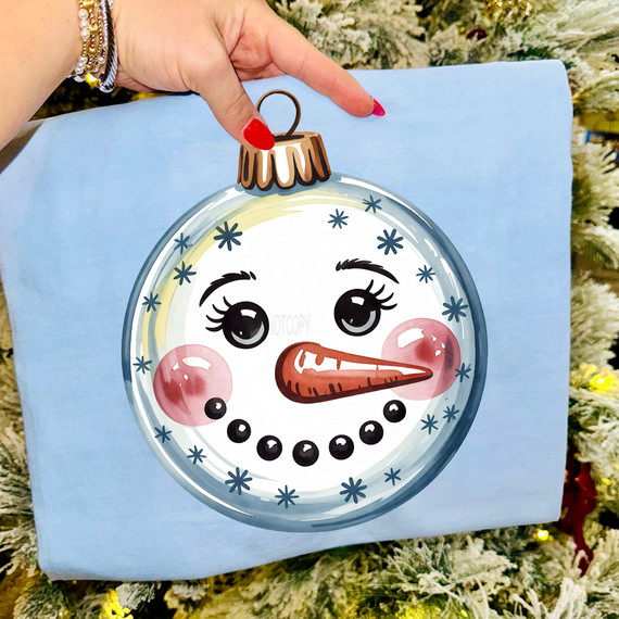 Snowman Ornament Face DTF Heat Transfer, cartoon snowman ornament with a happy face, rosy cheeks, and a carrot nose, on a light blue fabric background.