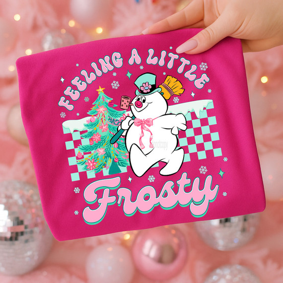 Felling A Little Frosty DTF Heat Transfer, pink fabric featuring a cartoon snowman with Christmas tree and the text 'Feeling a Little Frosty' in colorful letters.