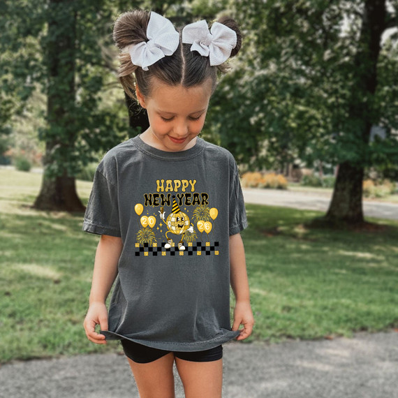 Happy New Year 2026 Retro Party Hat DTF Heat Transfer, young girl wearing a festive graphic t-shirt for New Year celebration with a cheerful design including a cartoon character, balloons, fireworks, and checkered patterns.
