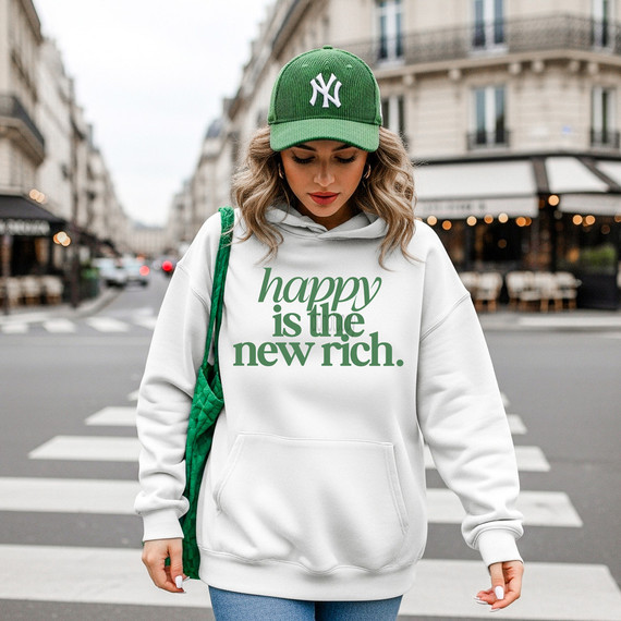 Happy Is The New Rich Green DTF Heat Transfer, a woman wearing a white hoodie with the green text 'happy is the new rich' and a green baseball cap with the New York Yankees logo, standing on a city street.
