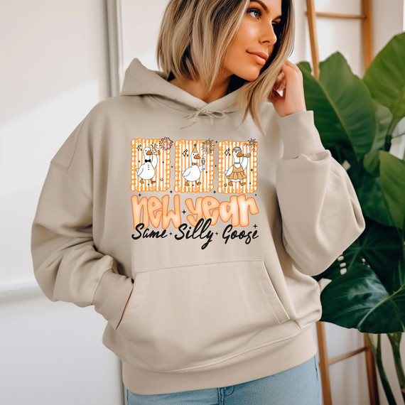 New Year, Same Silly Goose DTF Heat Transfer on a woman's beige hoodie with illustrated duck characters and festive decorations, celebrating the new year in a fun and cute style.
