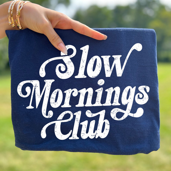 Slow Mornings Club WHITE DTF Heat Transfer, white vinyl transfer on a navy blue fabric with a hand holding the item outdoors.